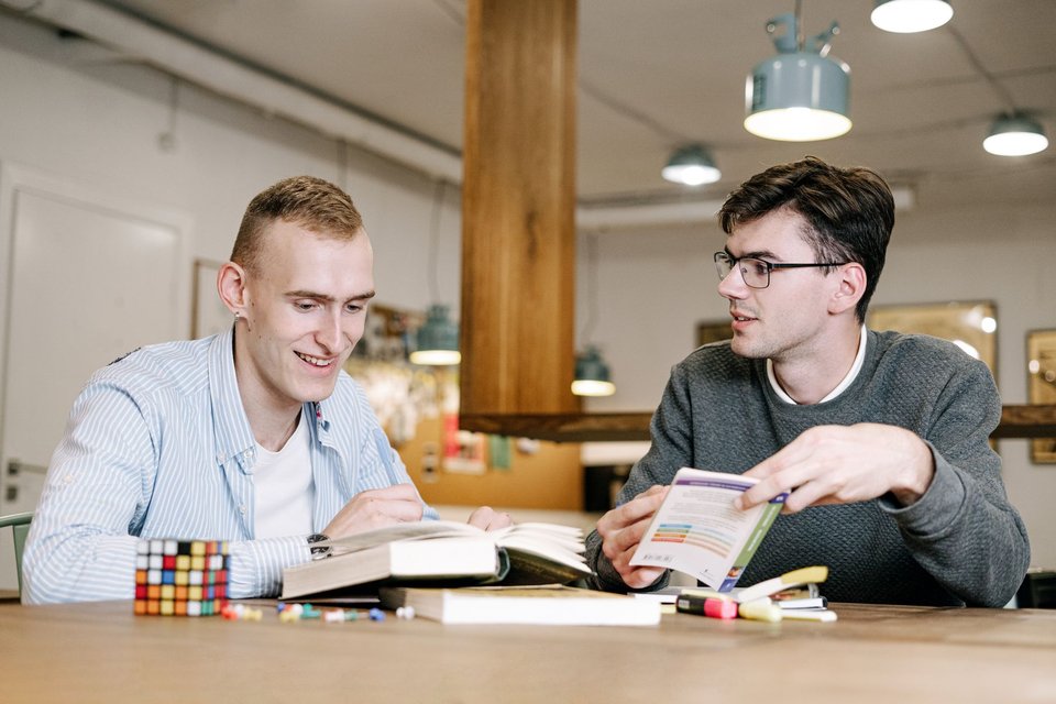 Two adults reviewing books and notes together at a table